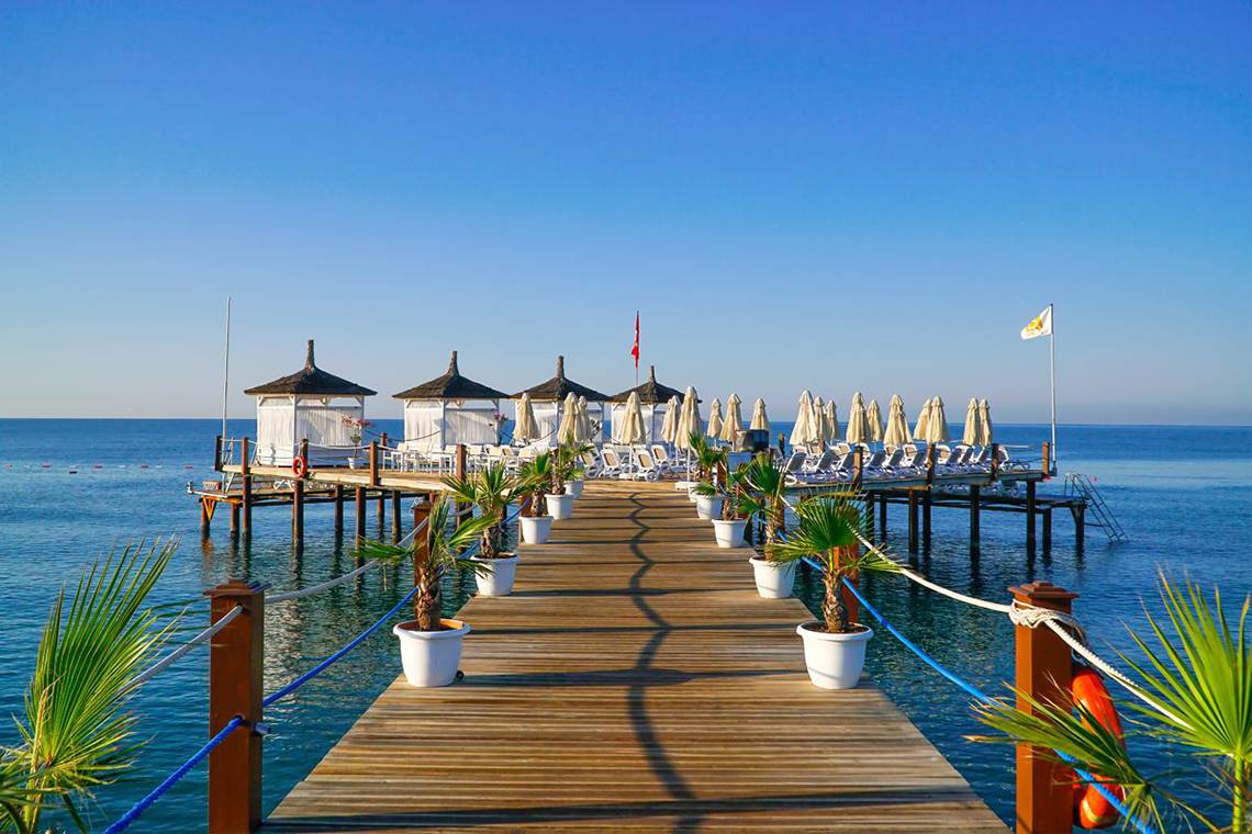 Anlegepier des Baia Lara Hotels mit Strandschirmen und Palmen an einem sonnigen Tag