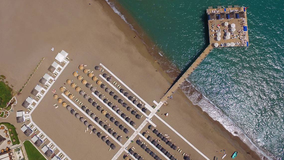Luftaufnahme des Baia Lara Hotels mit Strand und Pier, vielen Sonnenschirmen und Liegen
