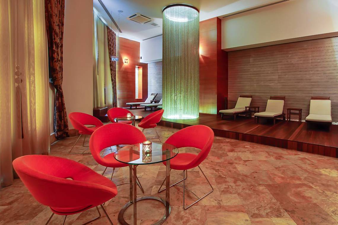 Loungebereich des Baia Lara Hotels mit roten Stühlen, Glastisch und Wasserfall.