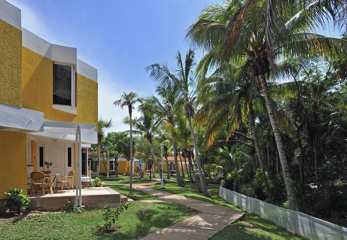 Außenansicht des Sol Palmeras Hotels mit gelben Gebäuden und Palmen.