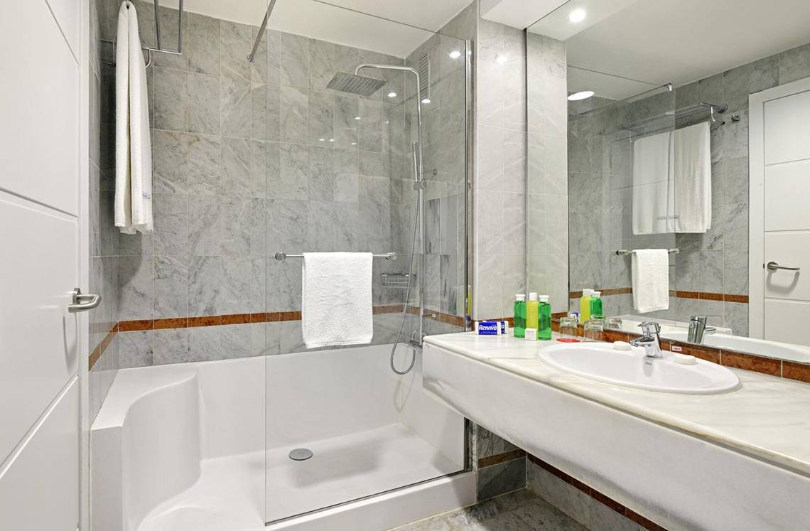 Badezimmer im Sol Palmeras Hotel mit Marmorfliesen, Badewanne, Dusche, Waschbecken und Spiegel.