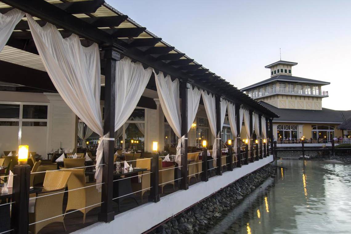 Terrasse des Sol Palmeras Hotels mit gepolsterten Stühlen und Tischen am Wasser.