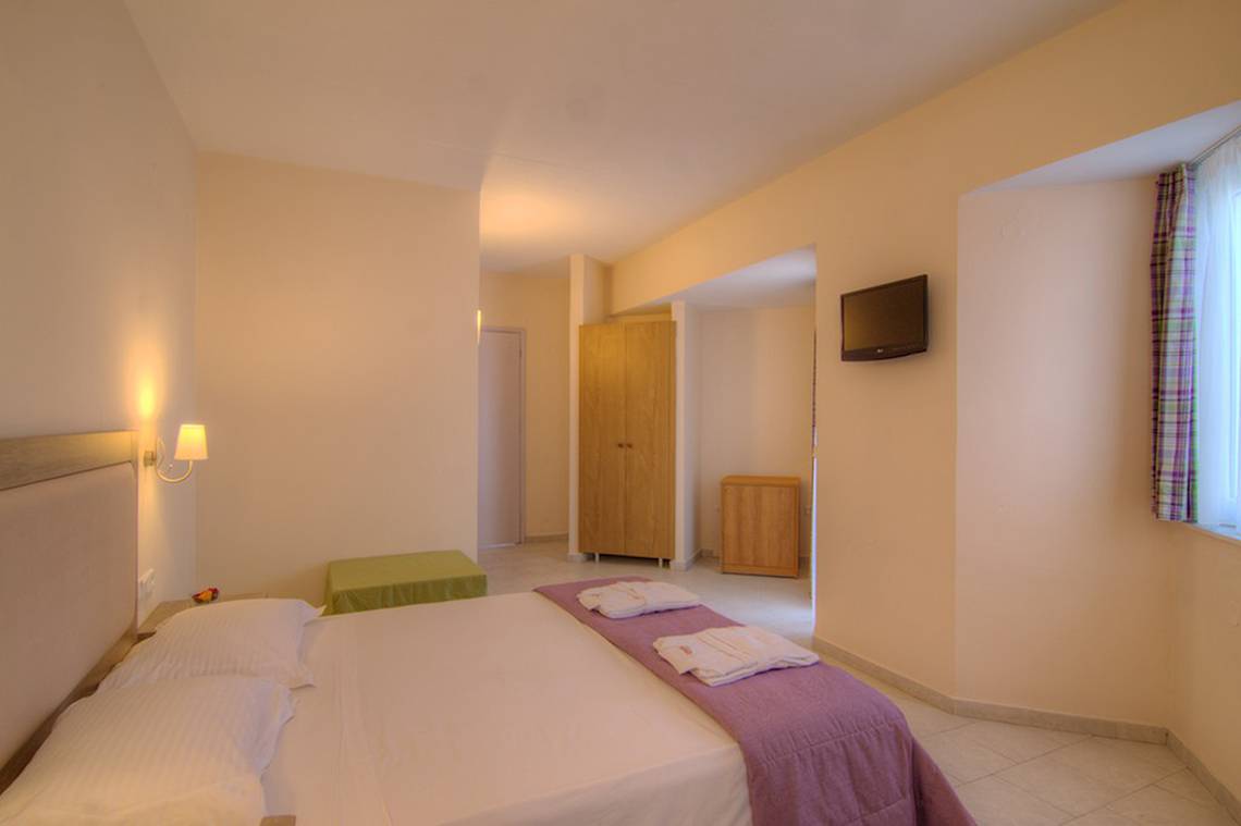 Ein geräumiges Hotelzimmer im Solimar Dias Hotel mit einem Bett, Kissen, Decken, einem Fernseher und einem Kleiderschrank.