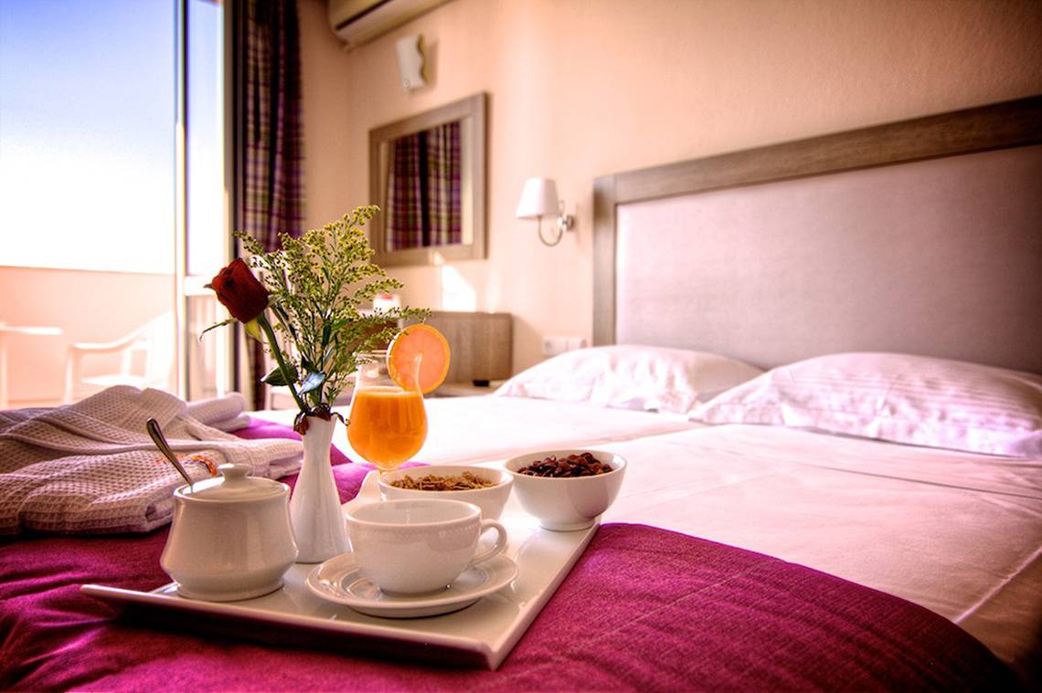 Frühstückstablett auf einem Bett im Solimar Dias Hotel mit Kaffee, Früchten und Brötchen.