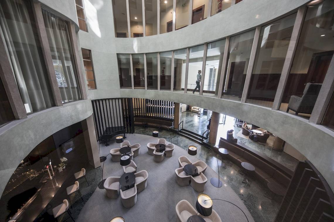 Innenansicht der Lobby des Gran Hotel Havana Barcelona mit Sitzgruppen und einer Person, die auf der oberen Ebene geht.
