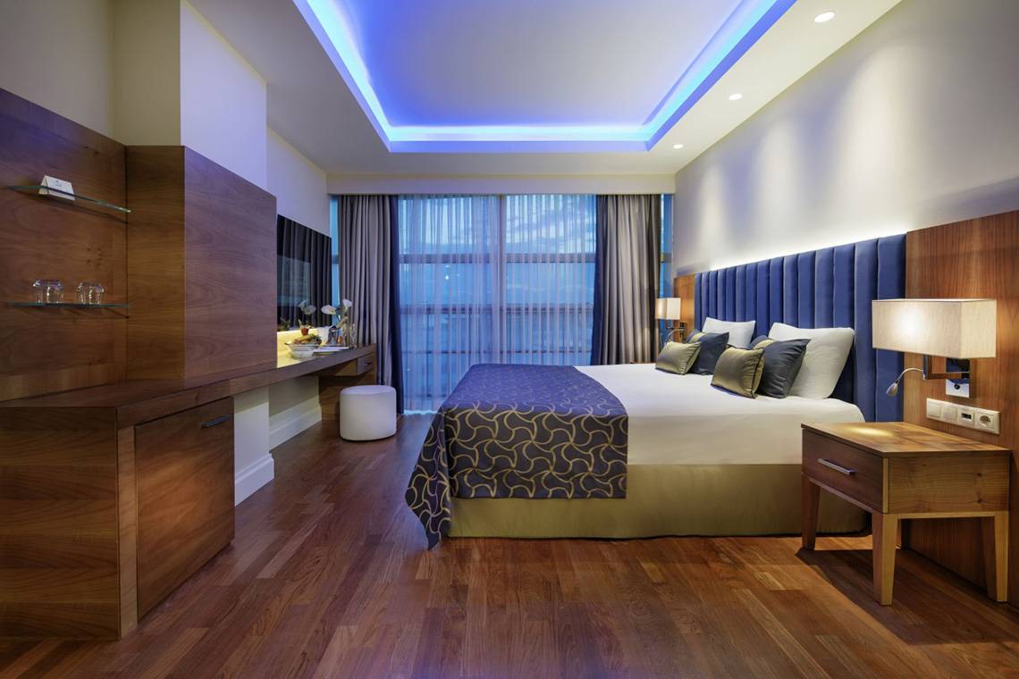 Innenansicht eines Schlafzimmers im Liberty Hotels Lara, mit einem großen Bett, Holzmöbeln und einer Aussicht.