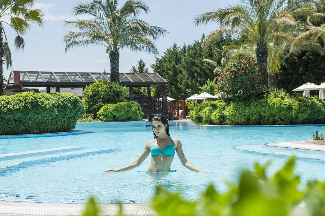 Frau in einem blauen Bikini schwimmt im Pool im Freien des Liberty Hotels Lara