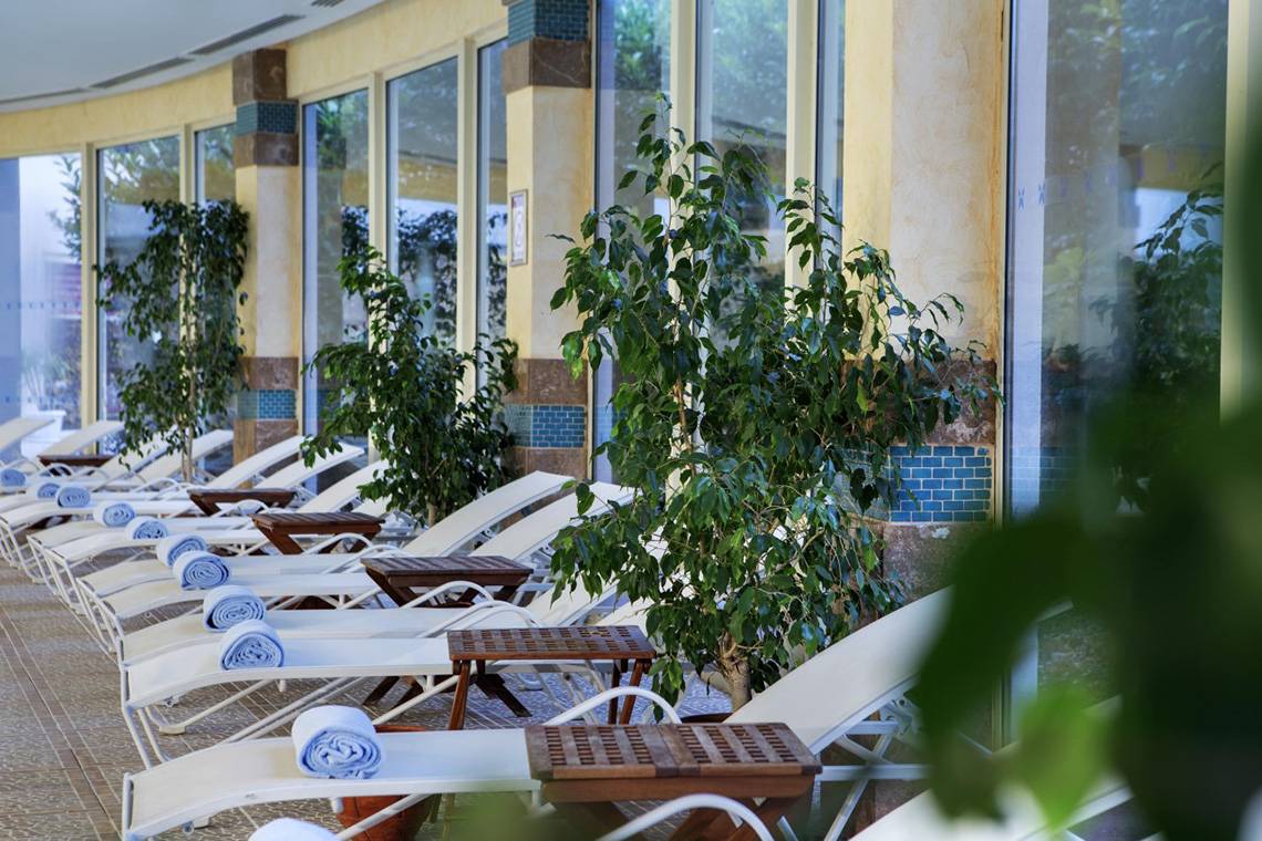 Reihe von weißen Liegen im Freien, neben Holztischen und Pflanzen, im Liberty Hotels Lara.