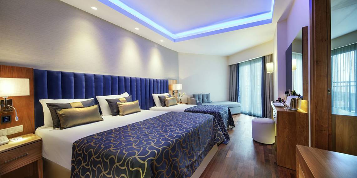Hotelzimmer mit zwei Betten und Sofa, Dekor im Innenraum, blaue Kissen und Decken, Möbel und Fernseher.