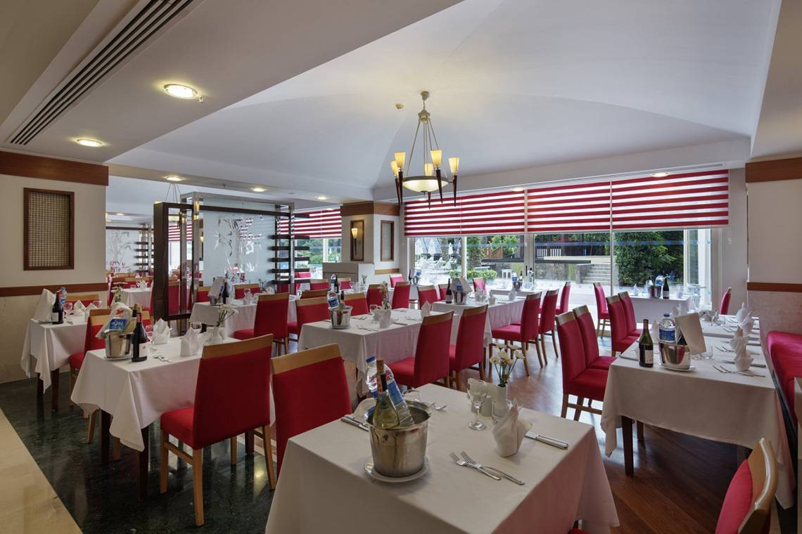 Innenansicht des Restaurants im Liberty Hotels Lara mit roten Stühlen und weißen Tischen.