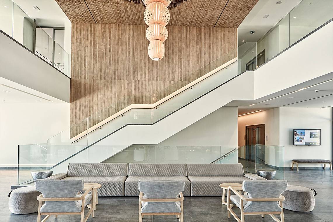 Innenansicht der Lobby des Atlantica Dreams Resort mit moderner Einrichtung, Couch, Stühlen, Tisch, Glasgeländer und Treppe.