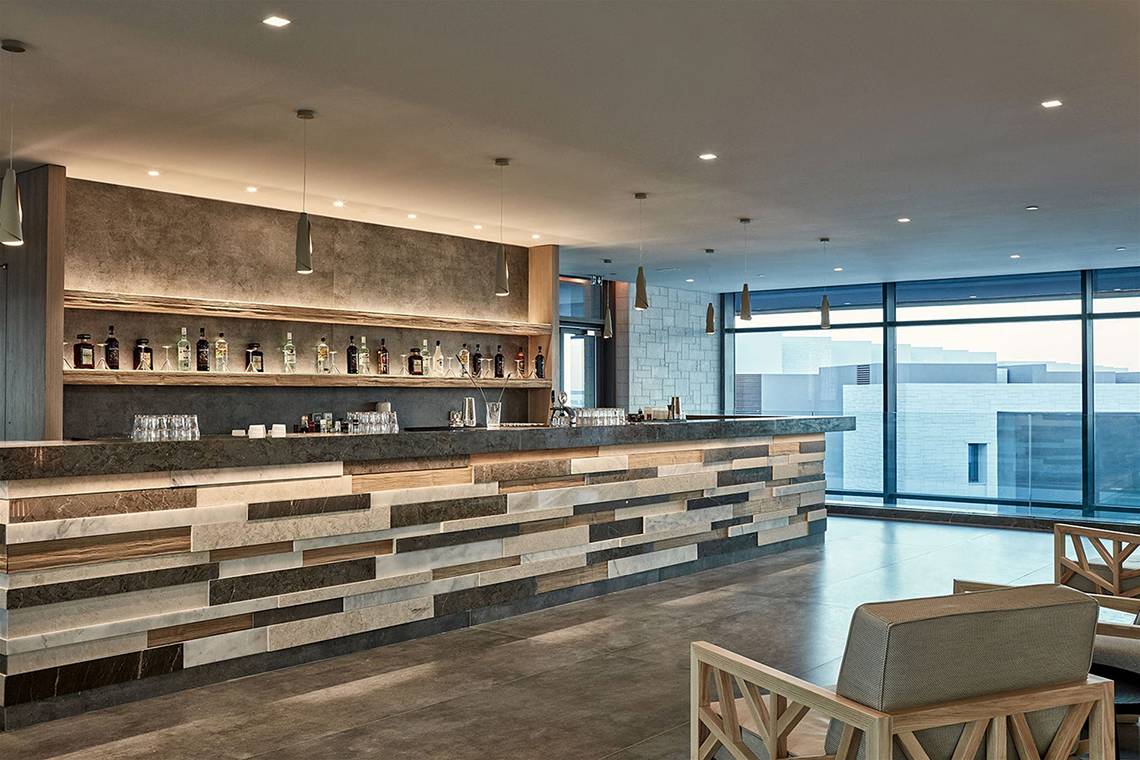 Innenansicht der Bar im Atlantica Dreams Resort mit einer Holz- und Marmortheke und großen Fenstern.