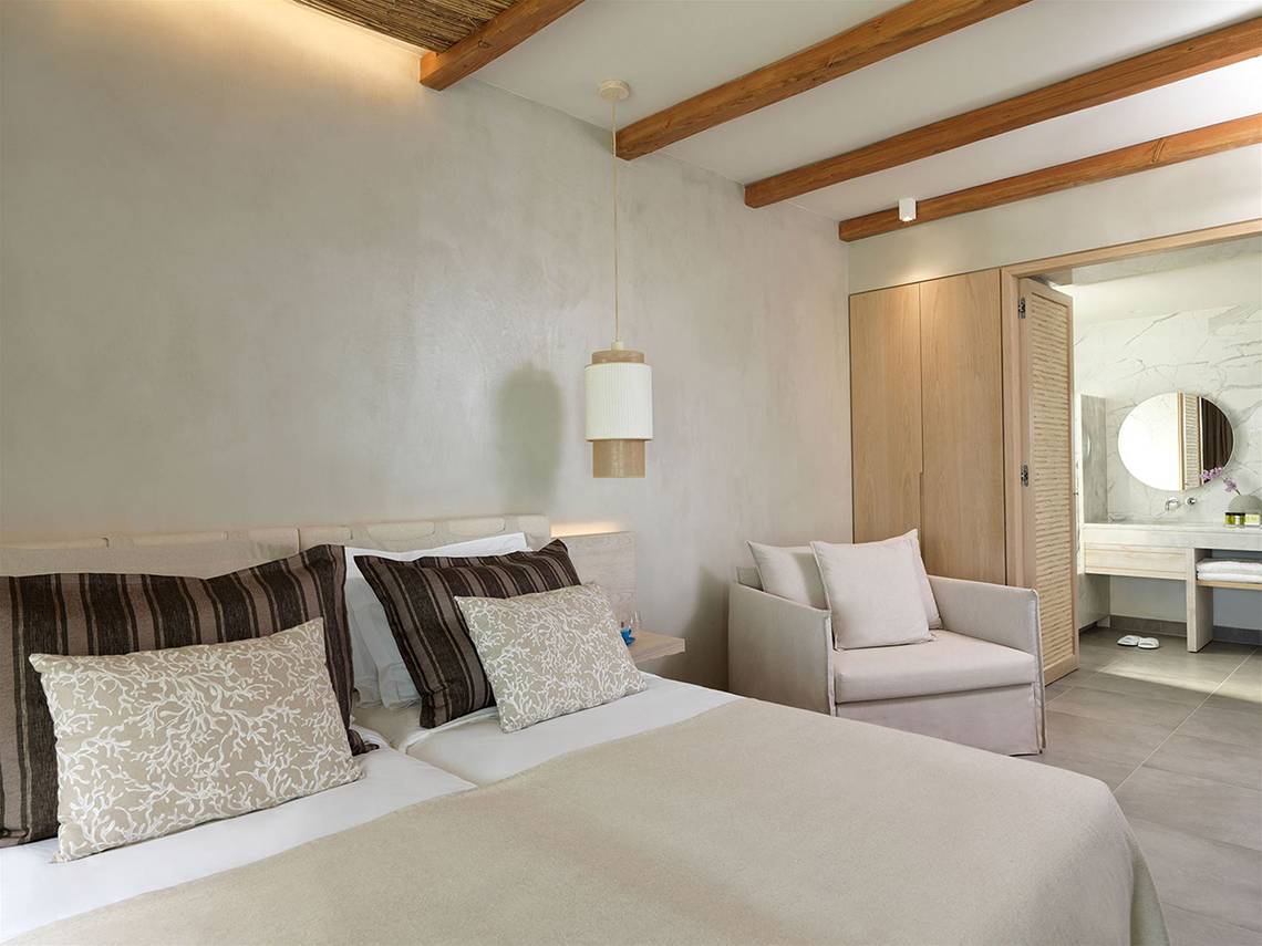 Ein modernes Schlafzimmer im Atlantica Dreams Resort mit weißen Wänden, Holzbalken und einem bequemen Bett.
