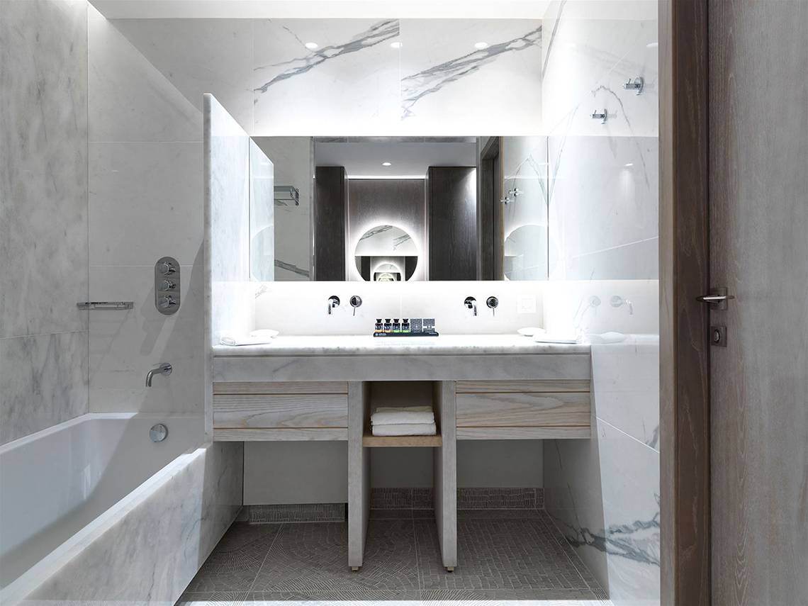 Ein modernes Badezimmer mit weißen Marmorwänden und Boden, einer Badewanne und einem Doppelwaschbecken mit Holzschubladen.