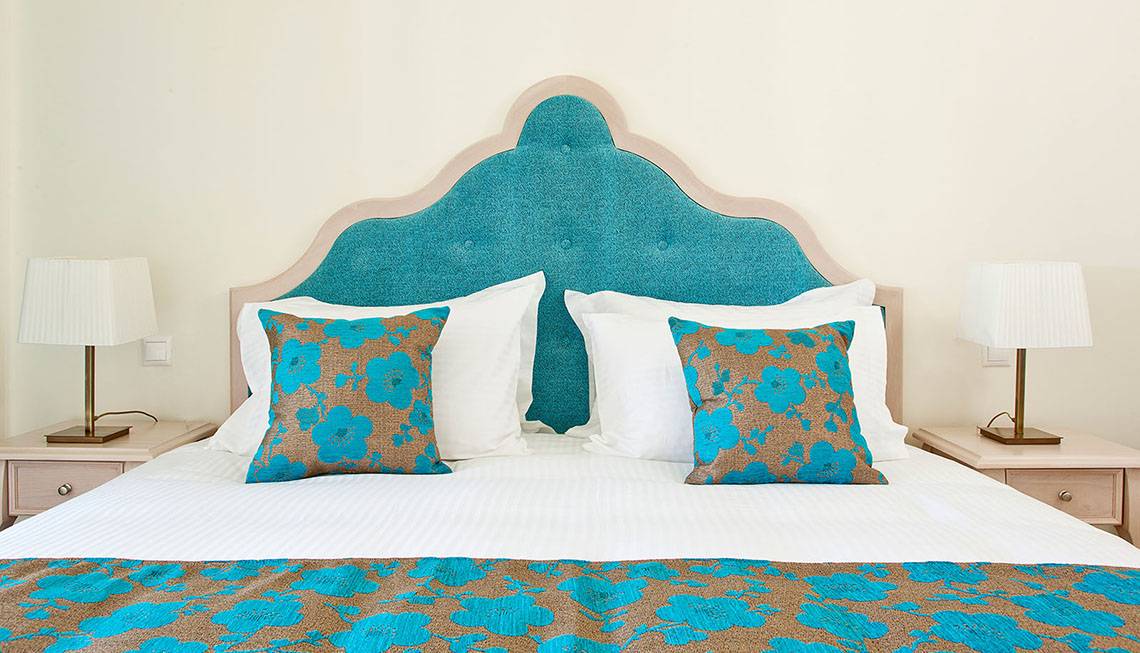 Hotelbett mit blauem Kopfteil und blau-braunen Kissen, weiße Kissen, zwei Lampen auf Nachttischen