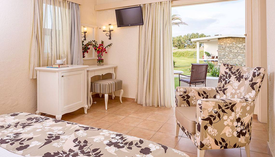 Hotelzimmer im Civitel Creta Beach mit offenem Fenster, Fernseher und Tisch mit Blumen.