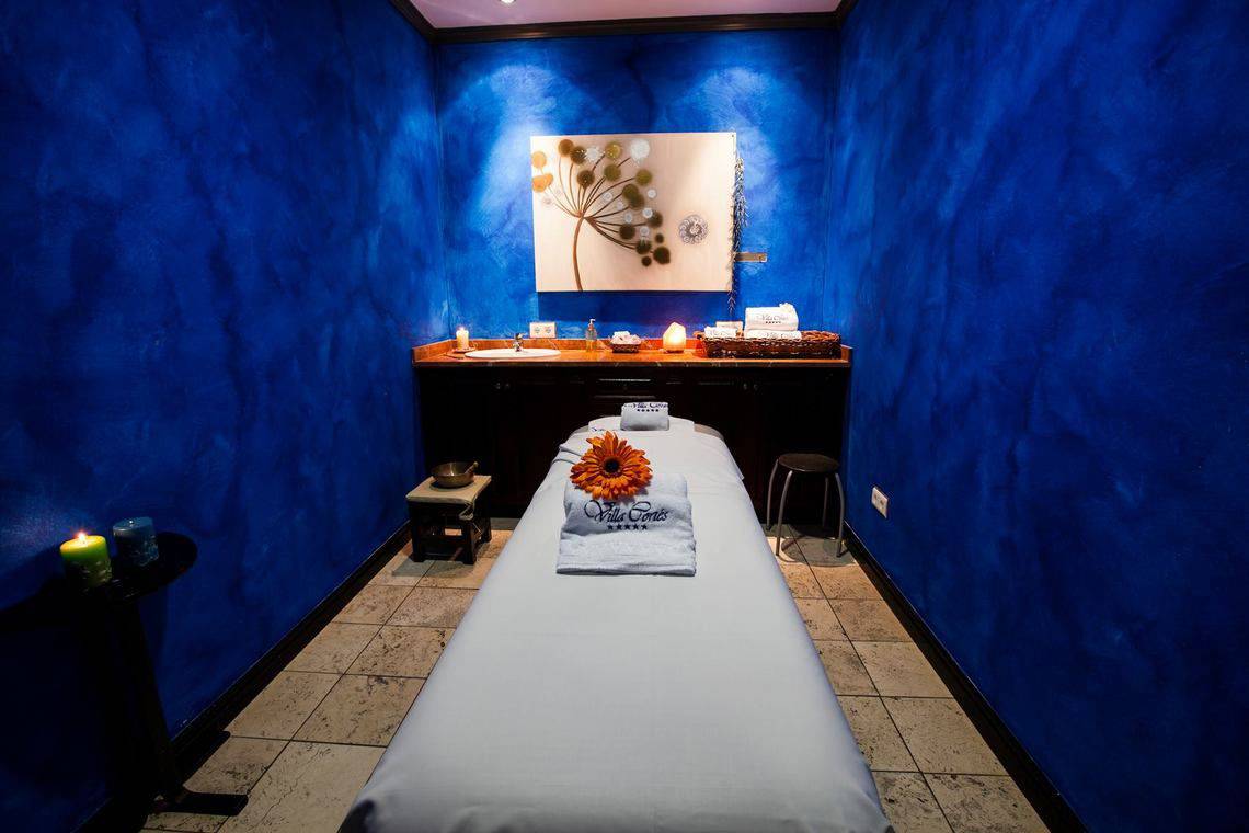 Massageraum im Hotel Europe Villa Cortes mit blauen Wänden, einem Behandlungstisch und Dekoration.