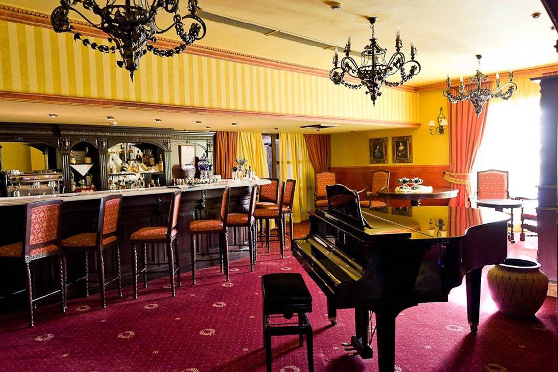 Barbereich mit Klavier in der Europe Villa Cortes mit roten Stühlen und Tisch.