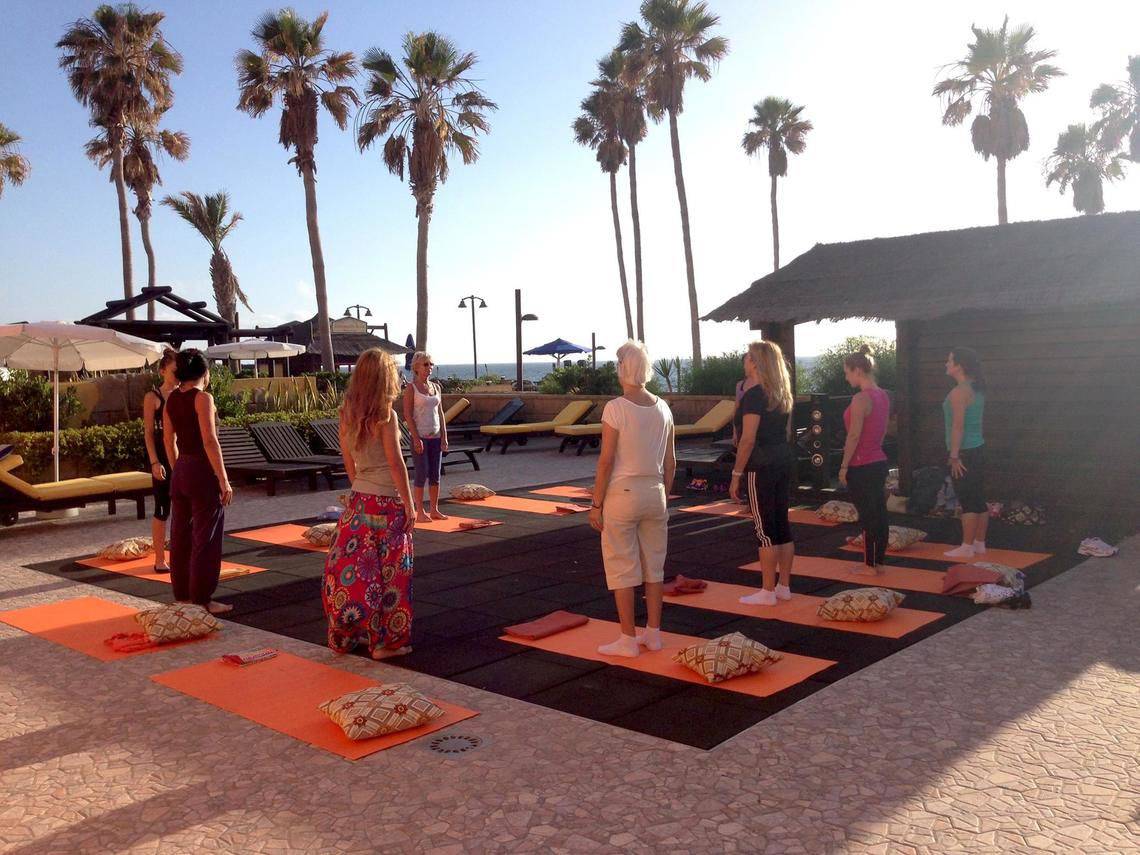 Yogakurs im Freien im Europa Villa Cortes mit Teilnehmern und Palmen im Hintergrund.