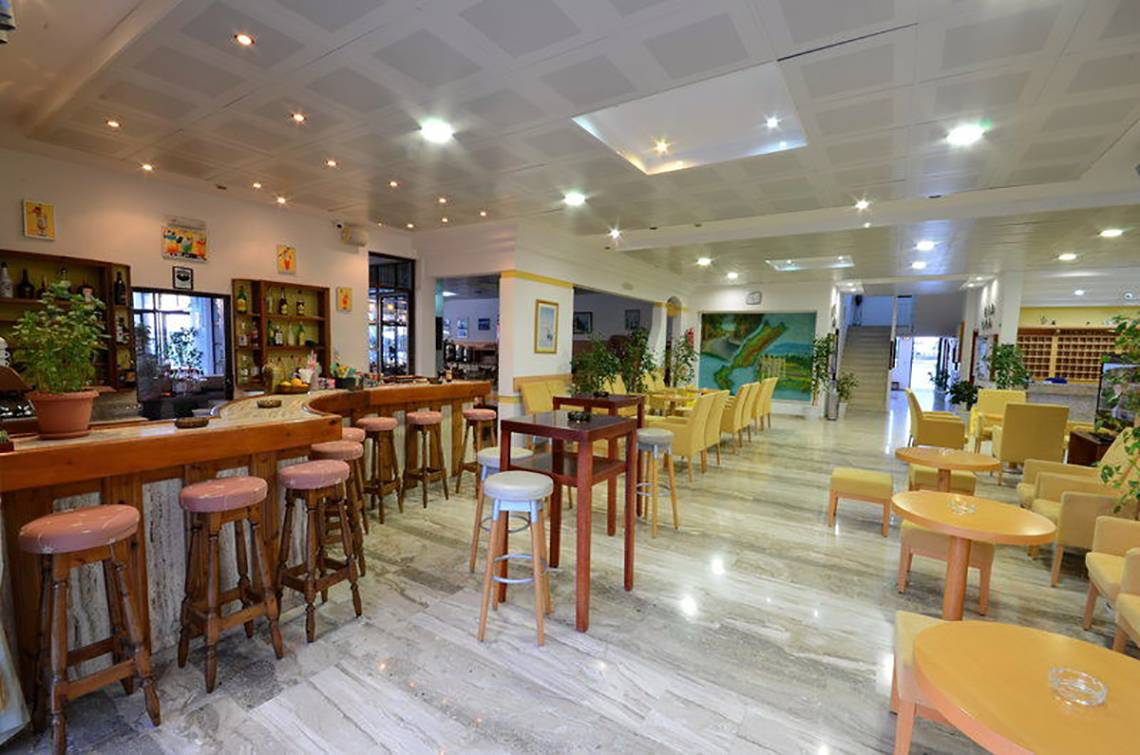 Die Lobby-Bar des Tropical Sol Hotels mit Barhockern, Tischen und gelb gepolsterten Stühlen.
