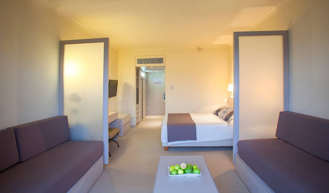 Innenansicht eines Hotelzimmers im Louis Imperial Beach mit Bett, Sofas und Tisch.