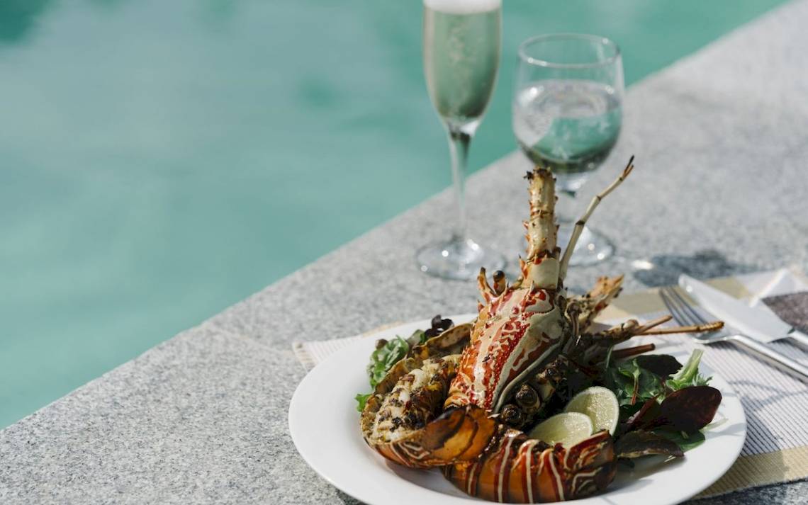 Gegrillter Hummer auf einem Teller mit Salat und Limetten auf einer Poolseite im Noku Maldives