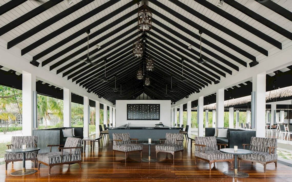 Loungebereich des Noku Maldives Hotels mit schwarzen und weißen Möbeln und Holzboden.