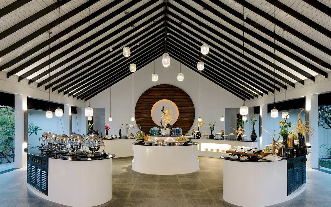 Innenansicht des Restaurants im Noku Maldives mit runden Tischen und hängenden Lampen.