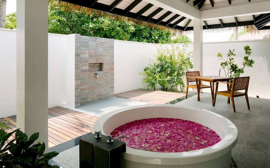 Außenbereich des Noku Maldives Hotels mit einer Badewanne voller Blumen und einem Tisch.