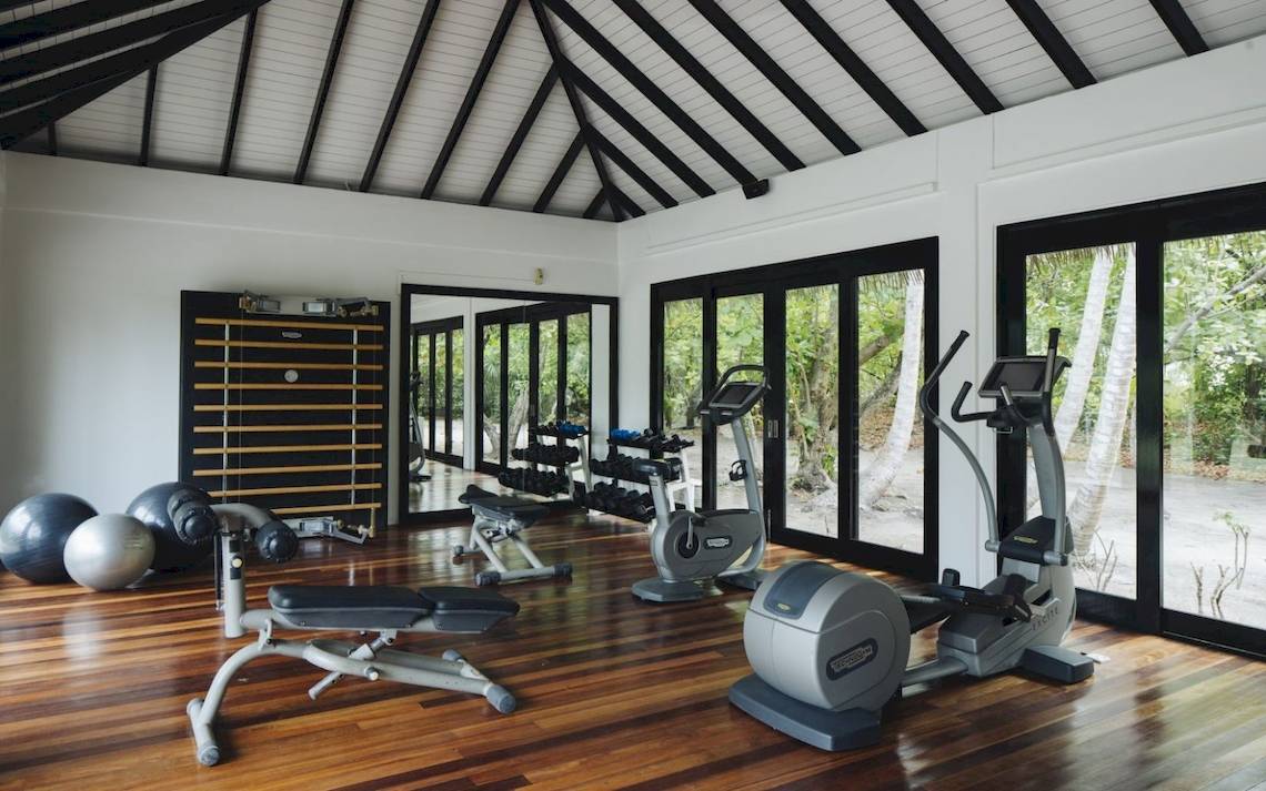Innenansicht des Fitnesscenters im Noku Maldives Hotel mit Geräten und Fenstern.