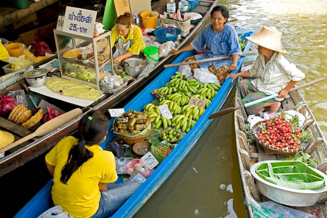 Mehrere bunte Boote auf einem Fluss in Thailand mit Verkäufern und Waren