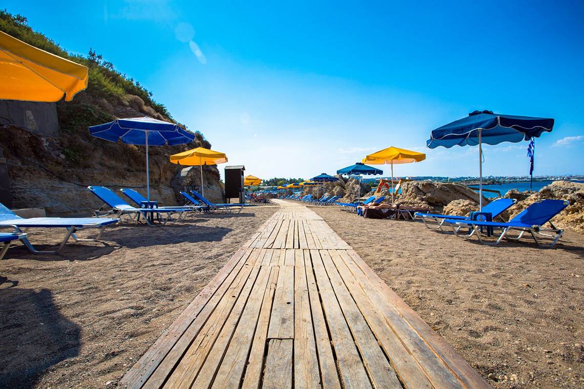 Strand des Kresten Palace Hotels mit Sonnenliegen und Sonnenschirmen an einem sonnigen Tag.