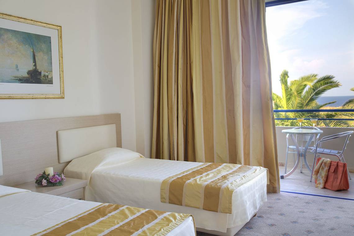 Zwei Betten in einem Zimmer im Kresten Palace Hotel mit einem Balkon, auf dem eine Tisch und Stühle stehen.