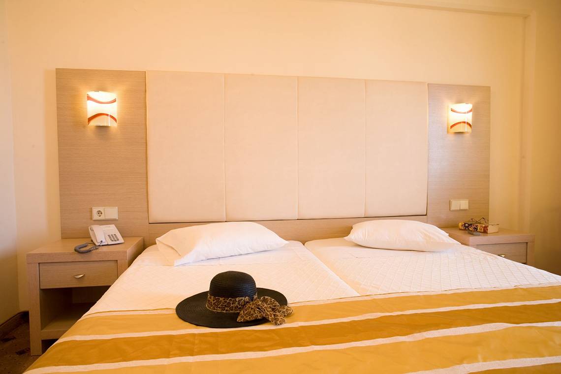 Doppelzimmer im Kresten Palace Hotel mit zwei Betten, weißen Kissen und einem schwarzen Hut auf dem Bett.