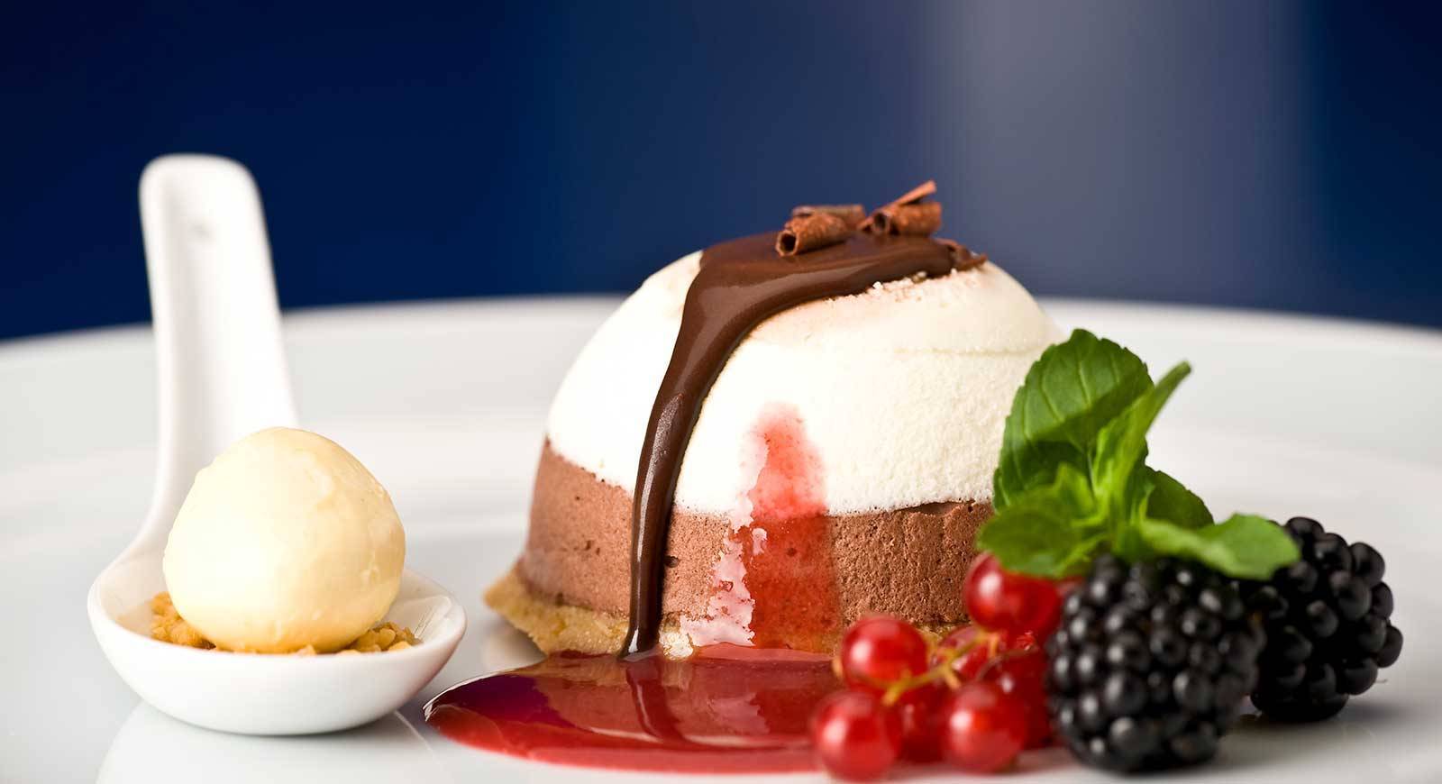 Ein Dessert mit Schokoladencreme, Beeren und Sahne auf einem weißen Teller.