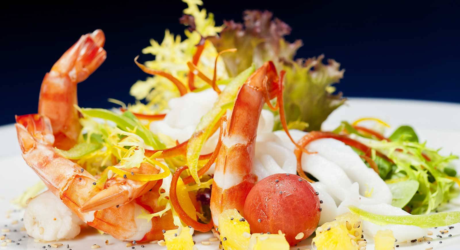 Nahaufnahme von Garnelen und Salat auf einem weißen Teller mit einer blauen Hintergrund.