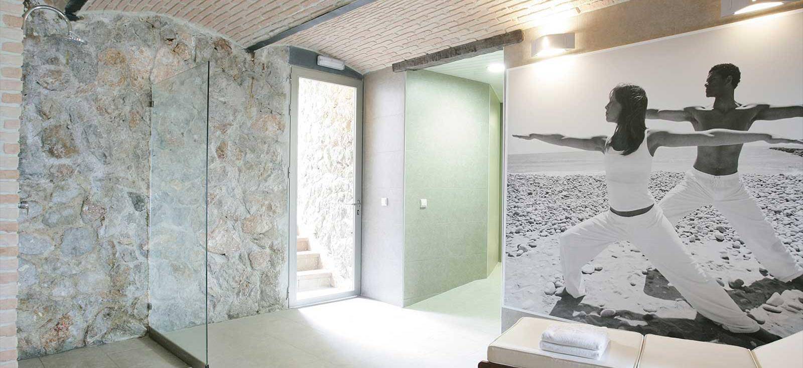 Innenansicht eines Yoga-Raums im Barcelo Illetas Albatros Hotel mit einer Steinwand und einem Foto von zwei Menschen in Yoga-Pose.