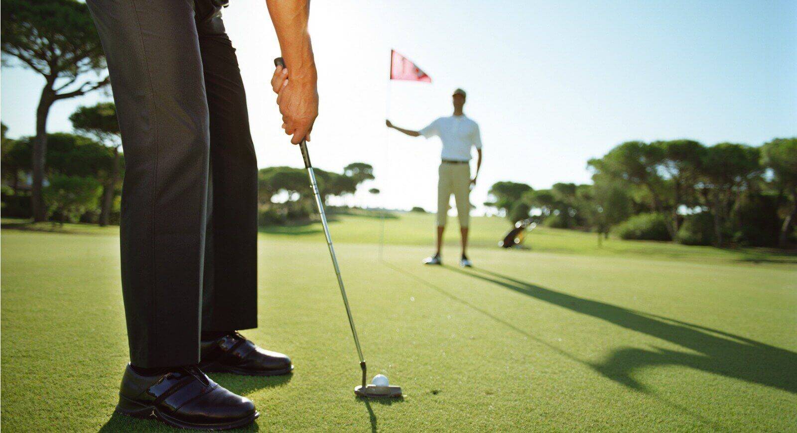 Golfer puttet auf dem Golfplatz mit einem Caddie im Hintergrund.