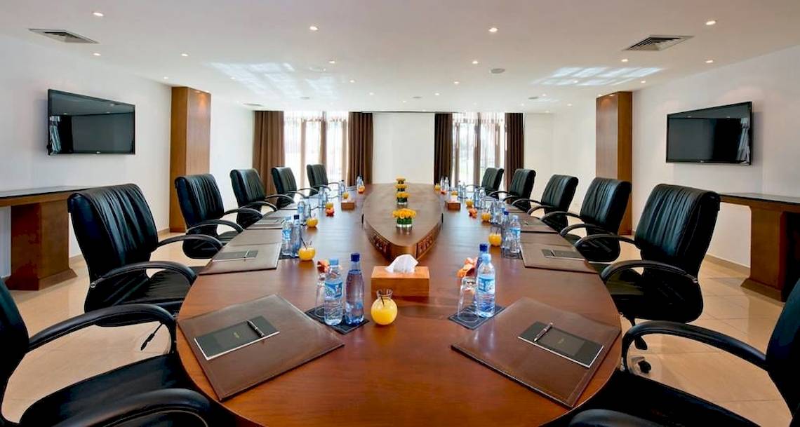 Ein Konferenzraum im Sofitel Agadir Royal Bay Resort mit einem großen Tisch, schwarzen Lederstühlen und Wasserflaschen.