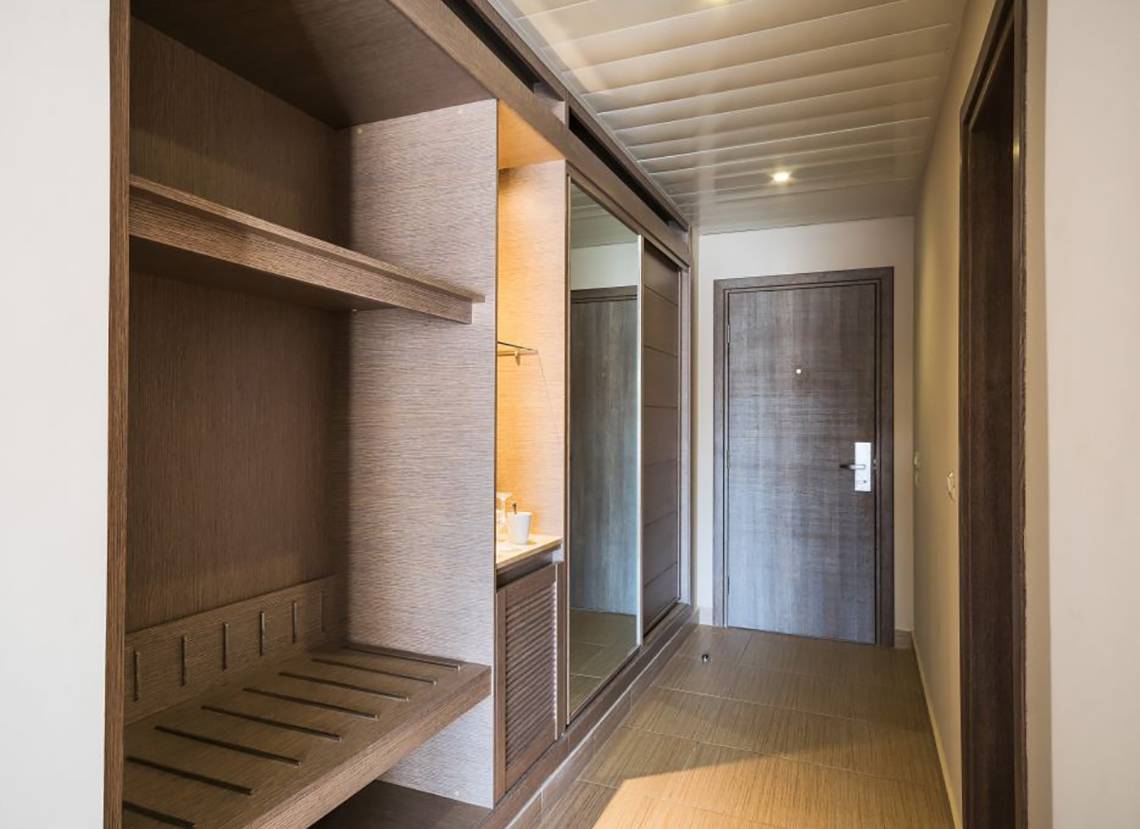 Eingangsbereich eines Hotelzimmers mit Garderobe, Waschbecken und Holzboden.
