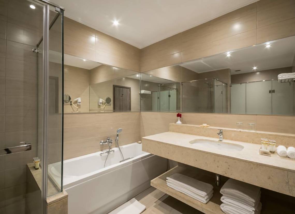 Ein modernes Badezimmer mit Badewanne, Waschbecken und Spiegeln im Steigenberger Alcazar Hotel.