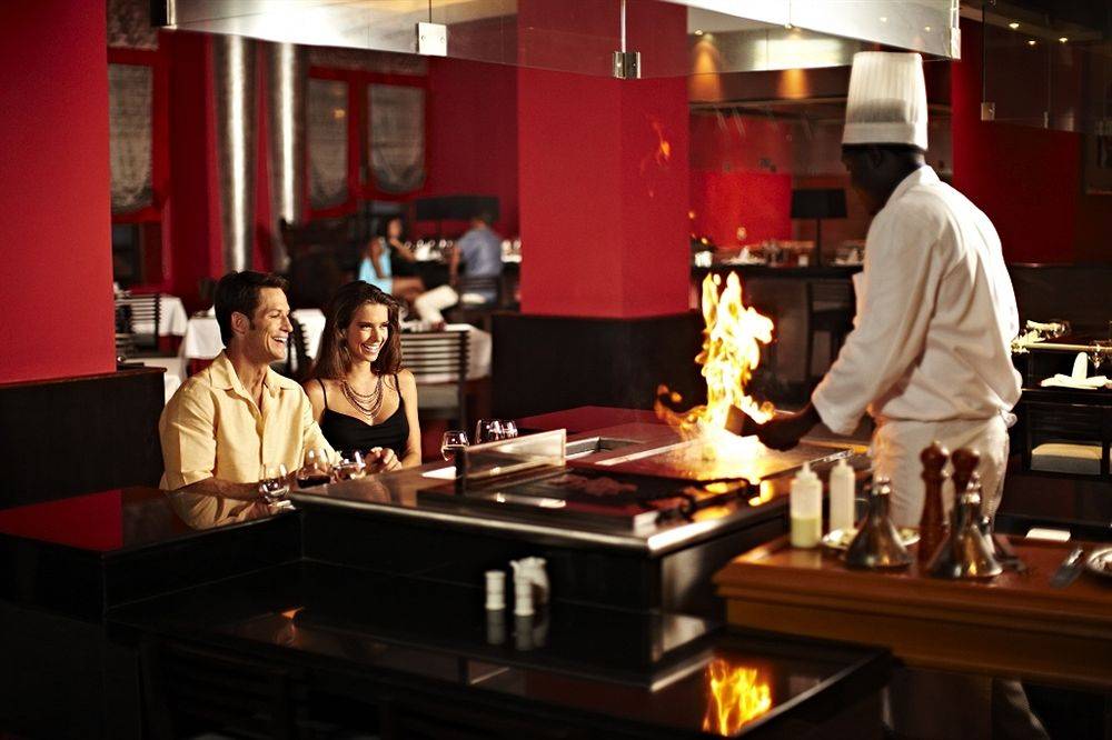 Ein Paar genießt das Essen im Restaurant des Iberostar Grand Rose Hall Hotels, während der Koch am Tisch Feuer macht.