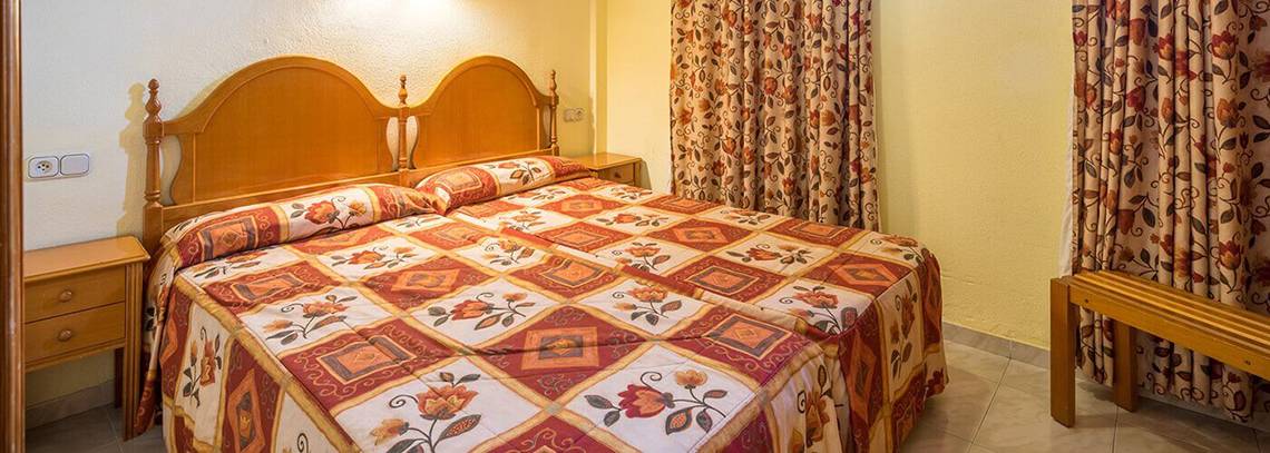 Doppelzimmer im Bluesea Callao Garden Hotel mit zwei Einzelbetten, Bettwäsche mit Blumenmuster, zwei Nachttischen und gelben Wänden.