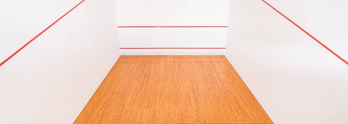 Leere Squashhalle mit roten Linien auf weißen Wänden und einem hölzernen Boden.