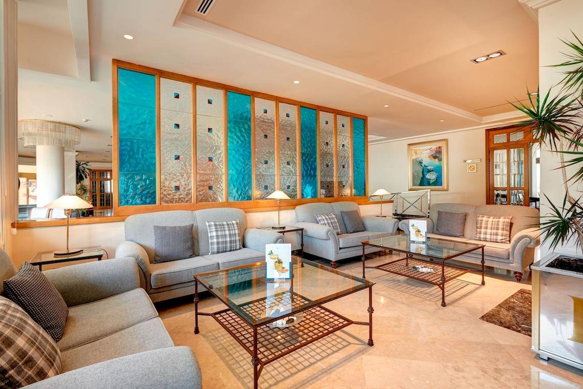 Lobby des Hipotels Hipocampo Playa Hotel mit blauen Glaswänden und modernen Möbeln.
