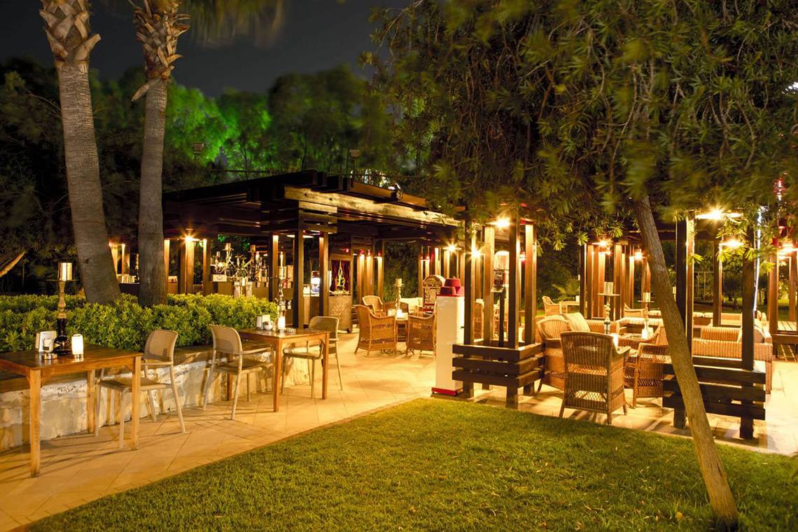 Außenbereich des Fame Residence Lara & Spa bei Nacht mit beleuchteten Tischen und Stühlen.