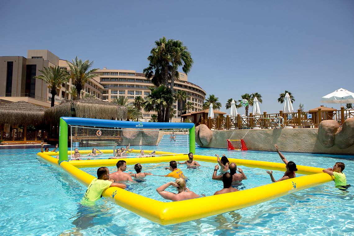 Gruppe von Erwachsenen spielt Volleyball im Pool des Fame Residence Lara & Spa Hotels.