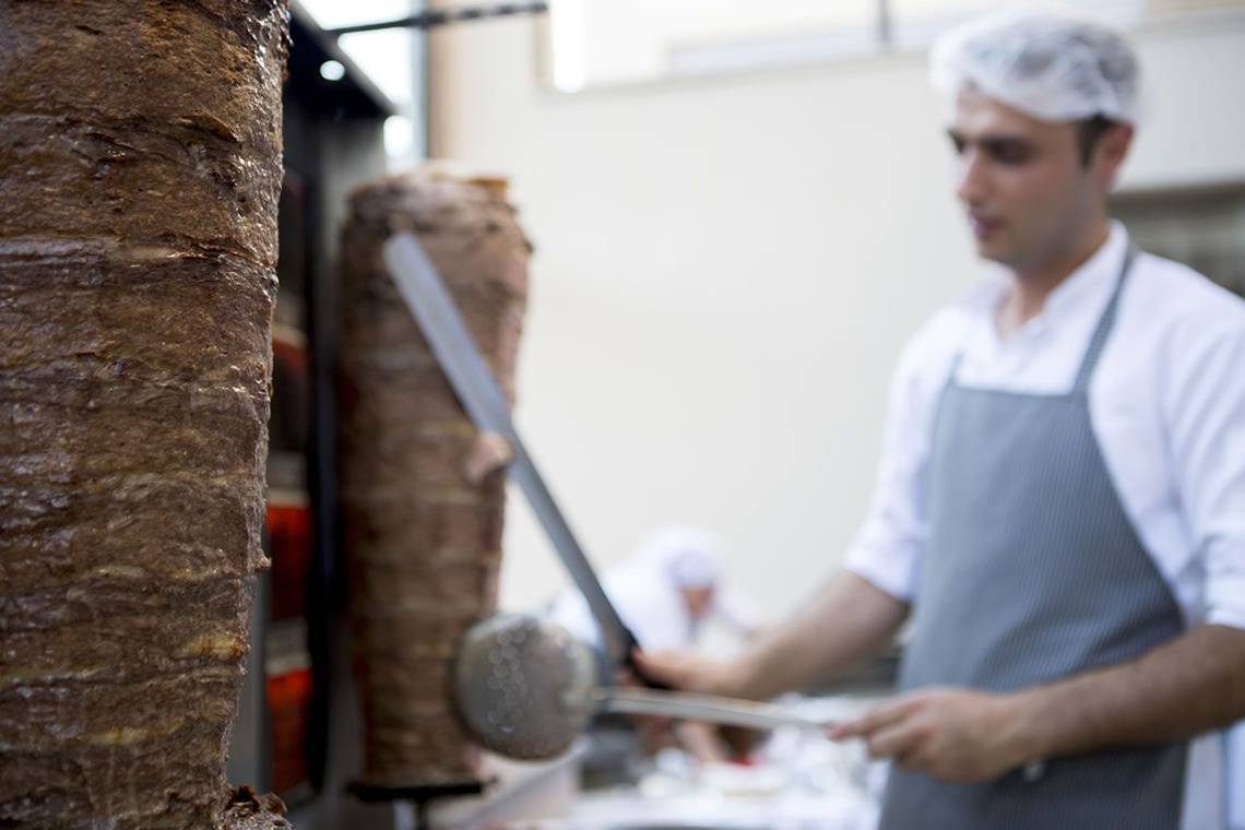 Mann schneidet gegrilltes Fleisch in der Küche des Fame Residence Lara & Spa Hotels.