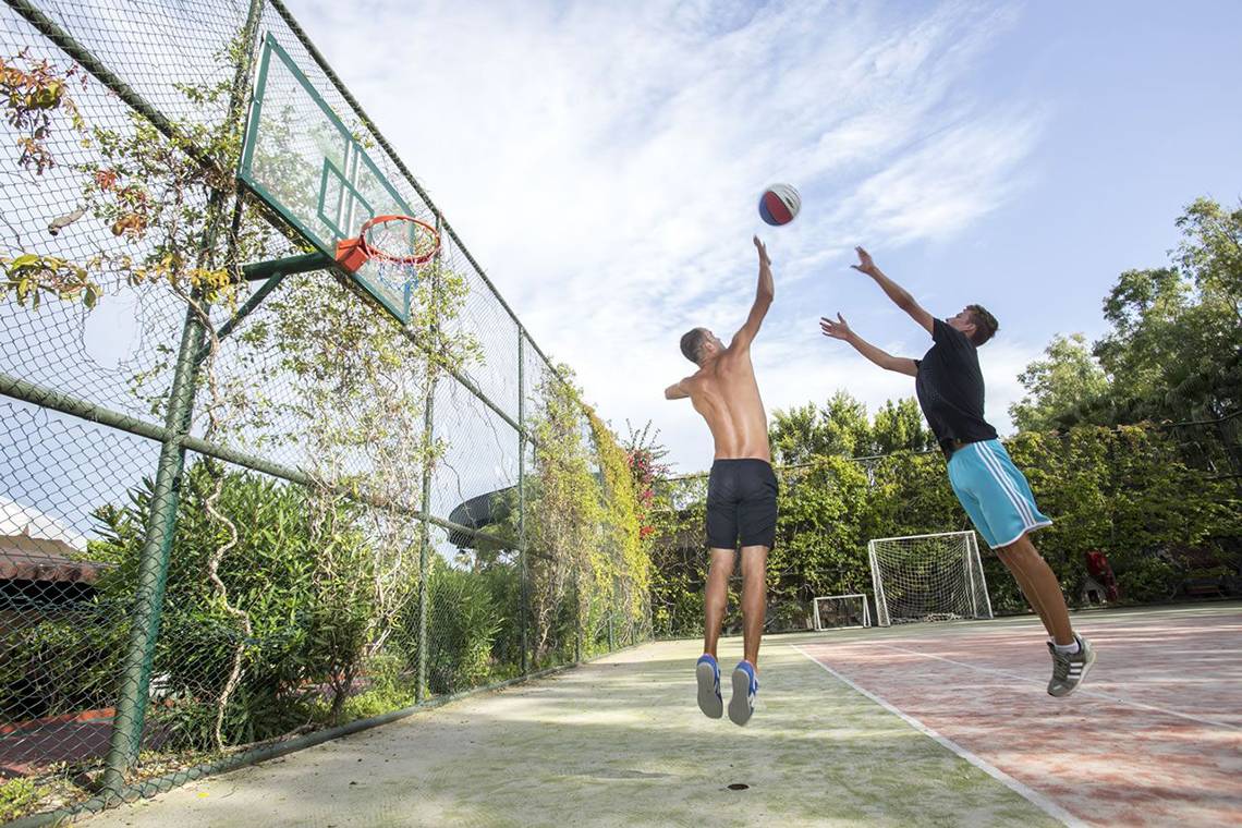 Zwei Männer springen, um einen Basketball zu werfen, auf einem Außensportplatz.
