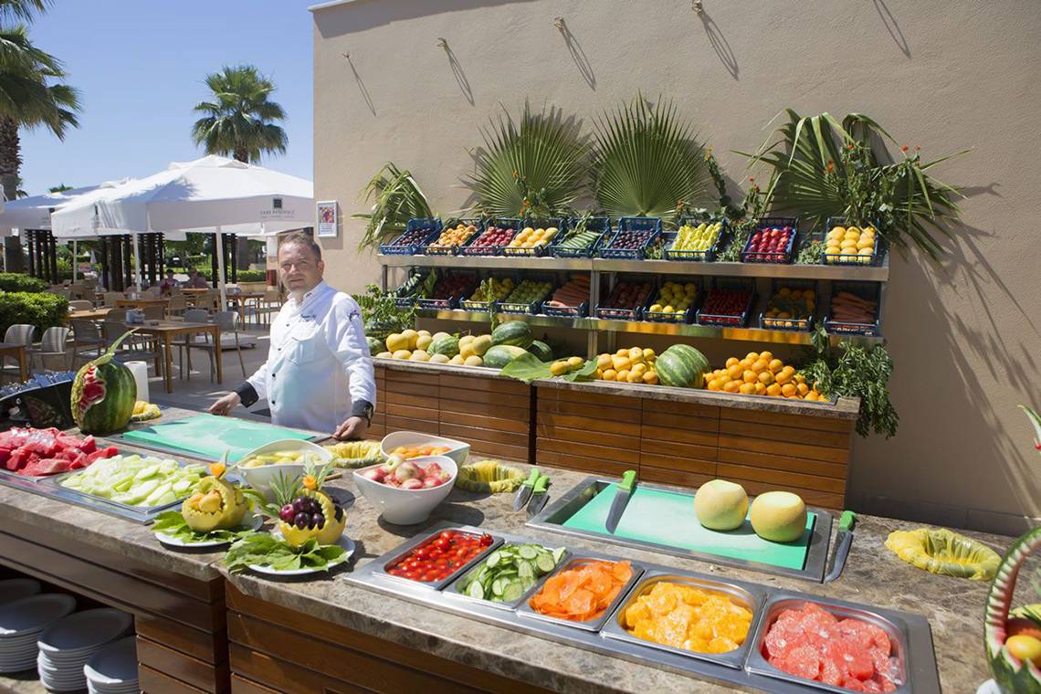 Ein Koch steht vor einem Buffet mit verschiedenen Früchten im Fame Residence Lara & Spa.